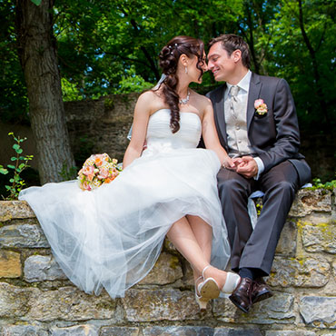 Hochzeit-in-Moeckmuehl-Schloss-Assumstadt-gluckliches-Brautpaar-sitzend-auf-einer-Wand-Fotograf-Natalja-Frei-Videograf-Sergej-Metzger